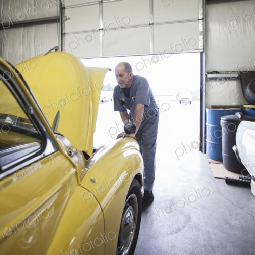 A mechanic looking under the bonnet of a bright yellow Morris Minor English classic car. A mechanic looking under the bonnet of a bright yellow Morris Minor English classic car.