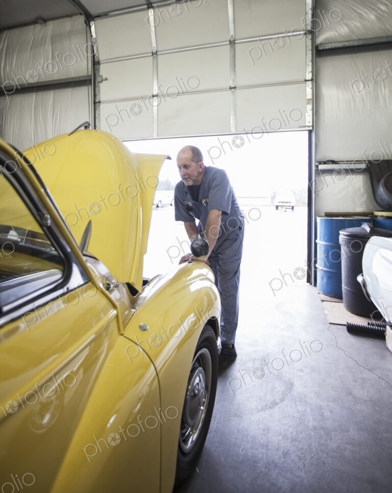 A mechanic looking under the bonnet of a bright yellow Morris Minor English classic car.