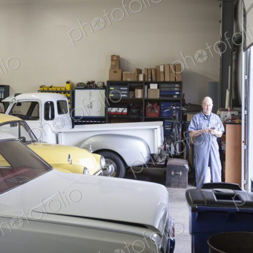 A mechanic standing in an auto repair shop, with a line of classic cars.