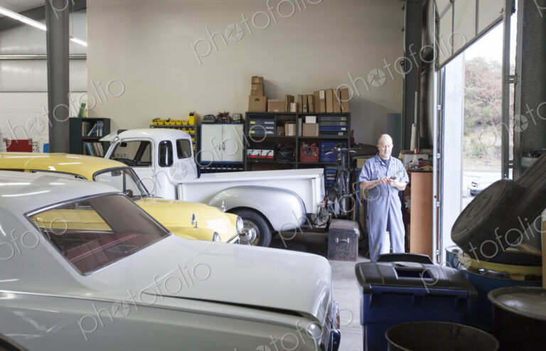 A mechanic standing in an auto repair shop, with a line of classic cars.