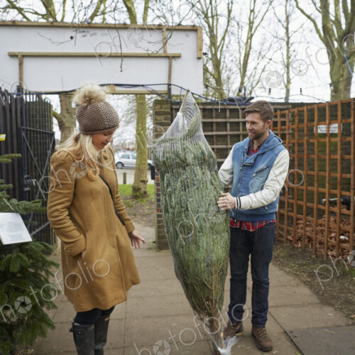A member of staff carrying a traditional pine tree, Christmas tree talking to a woman… A member of staff carrying a traditional pine tree, Christmas tree talking to a woman…