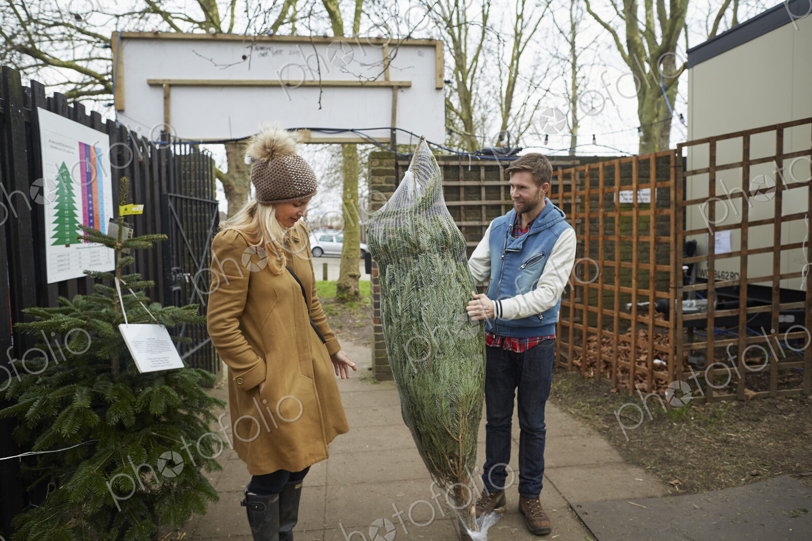 A member of staff carrying a traditional pine tree, Christmas tree talking to a woman…