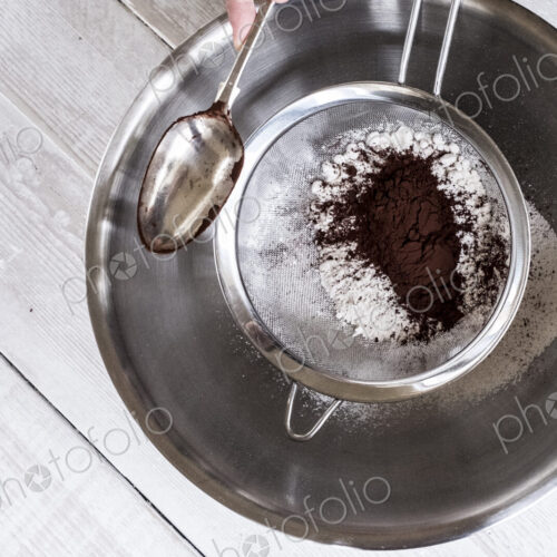 A metal bowl with ingredients and a sieve with cocoa powder. A metal bowl with ingredients and a sieve with cocoa powder.