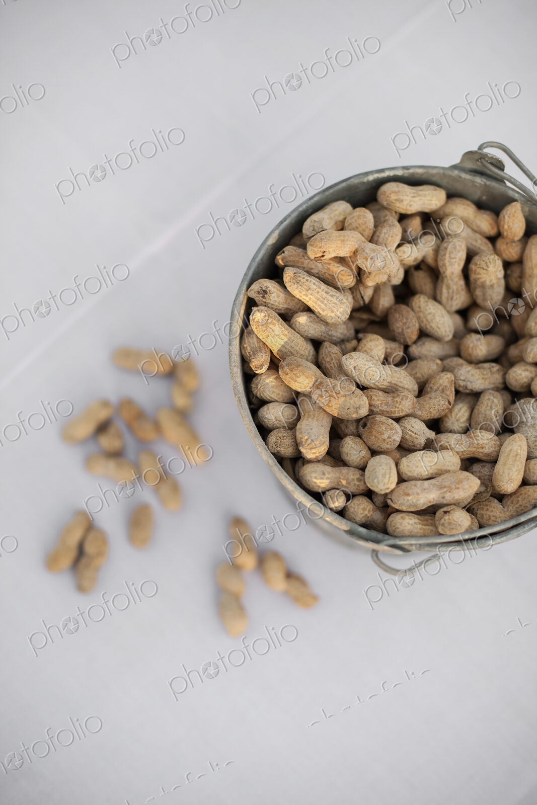 A metal container with a handle. Peanuts with their husks on. Organic nuts, Arachis…
