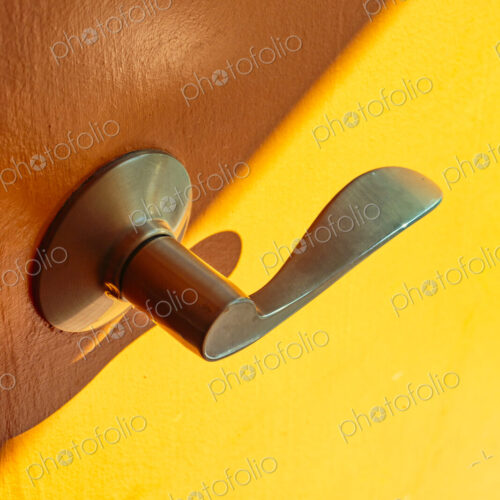 A metal door handle in brass colour on a wooden door and yellow background.