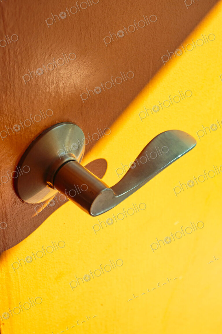 A metal door handle in brass colour on a wooden door and yellow background.