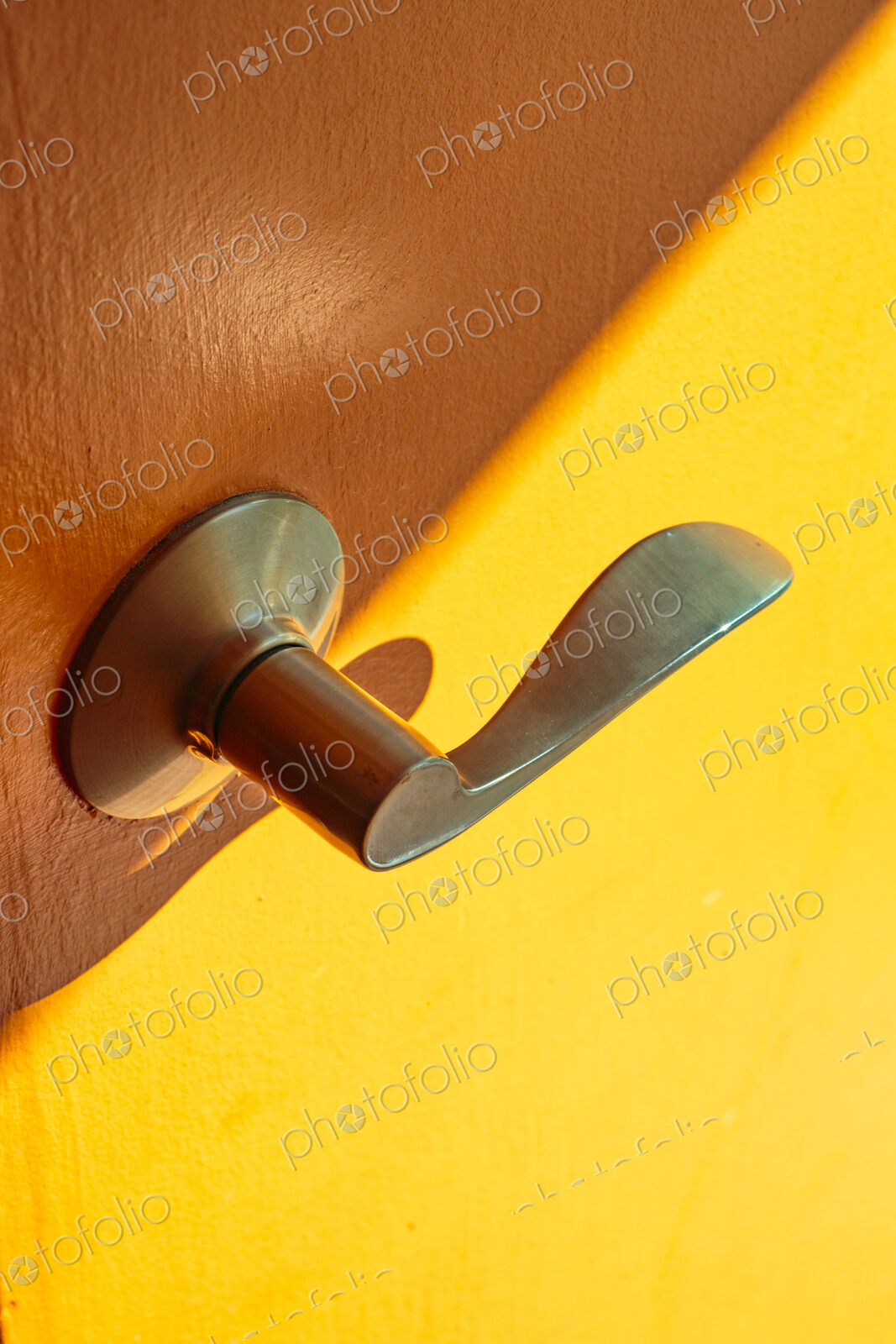 A metal door handle in brass colour on a wooden door and yellow background.