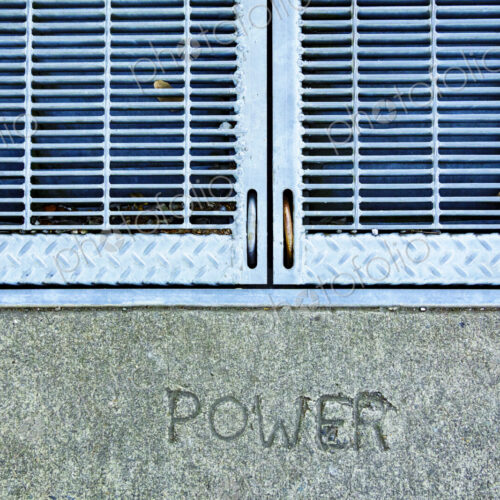 A metal grille over a power utility vault on a wall, the word Power embossed in stone. A metal grille over a power utility vault on a wall, the word Power embossed in stone.