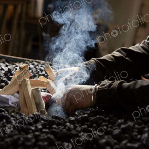 A metal worker lighting a furnace fire using wooden sticks and paper on top of a heap… A metal worker lighting a furnace fire using wooden sticks and paper on top of a heap…