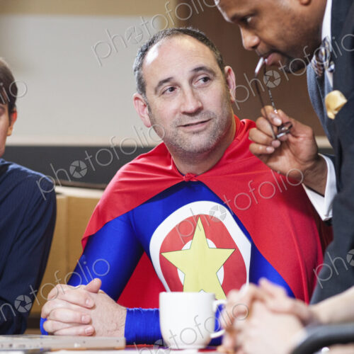 A middle aged caucasian office super hero in a meeting with his staff. A middle aged caucasian office super hero in a meeting with his staff.