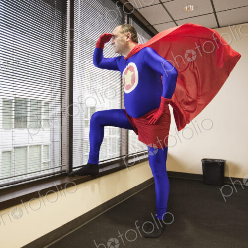 A middle aged caucasian office super hero stands at a window and ponders his next… A middle aged caucasian office super hero stands at a window and ponders his next…