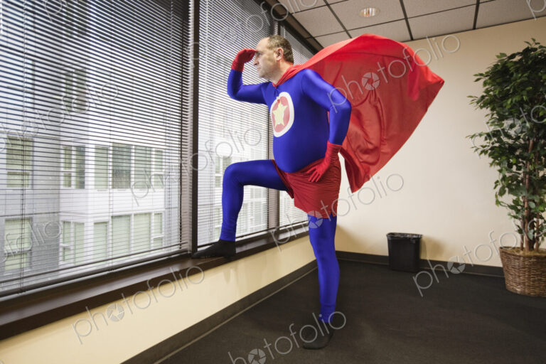 A middle aged caucasian office super hero stands at a window and ponders his next…