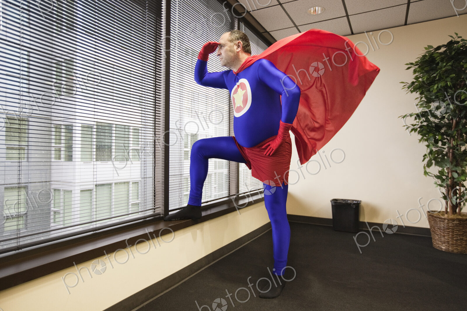 A middle aged caucasian office super hero stands at a window and ponders his next…