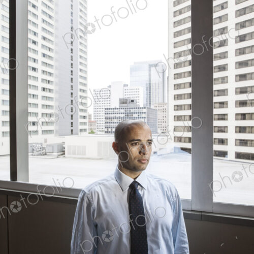 A middle eastern businessman by window with a view of tall office buildings.