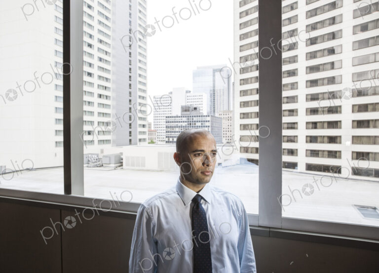 A middle eastern businessman by window with a view of tall office buildings.
