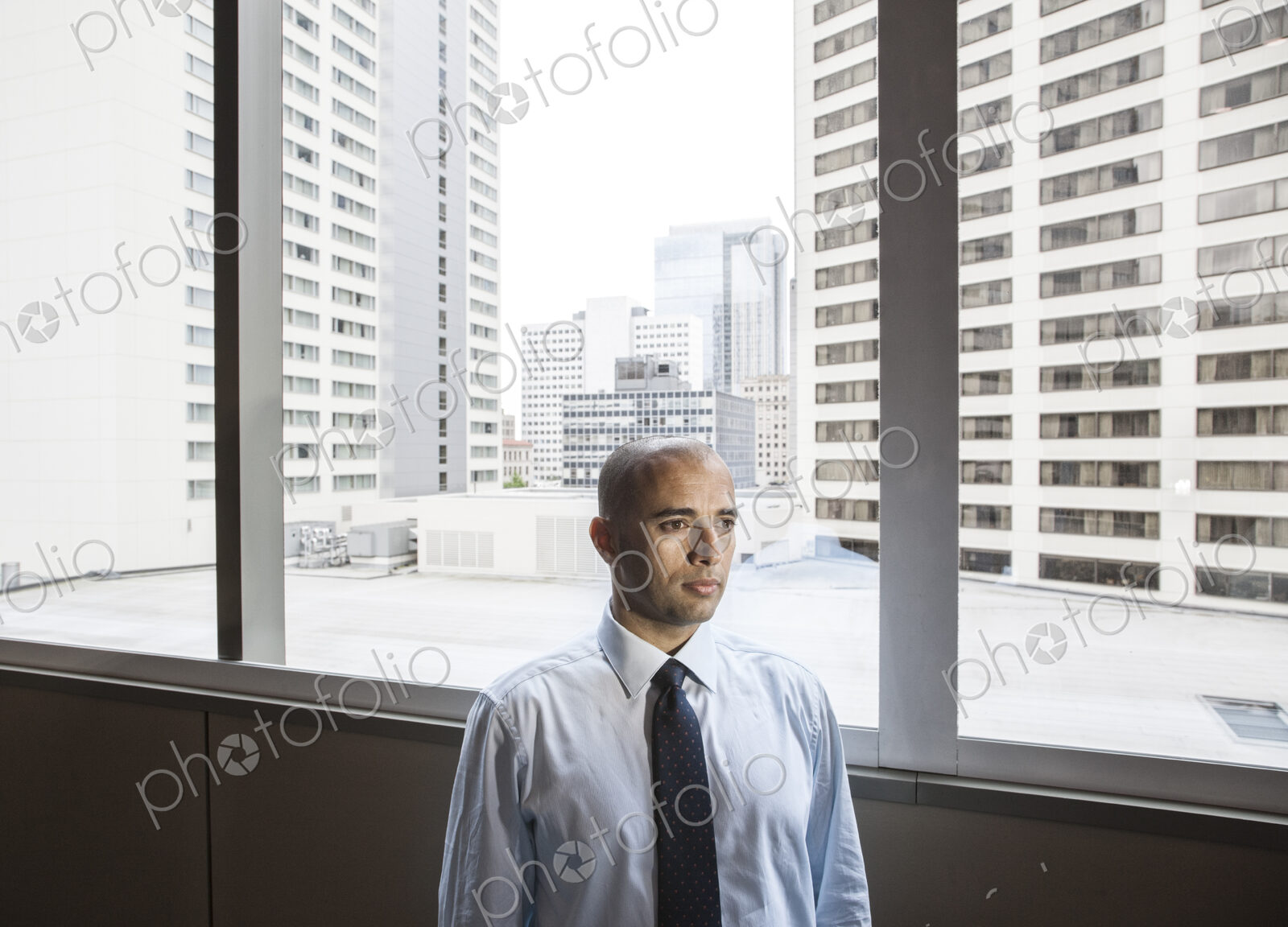 A middle eastern businessman by window with a view of tall office buildings.