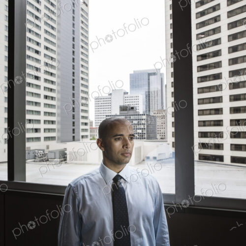 A middle eastern businessman by window with a view of tall office buildings.