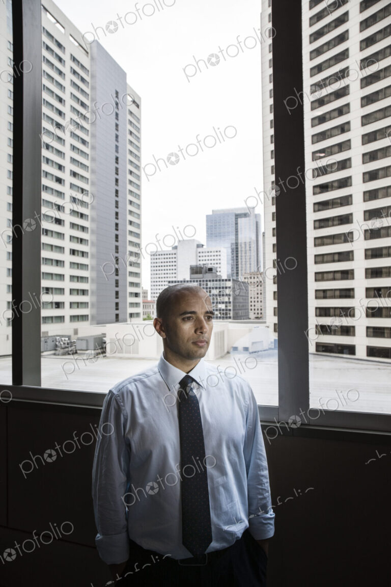 A middle eastern businessman by window with a view of tall office buildings.