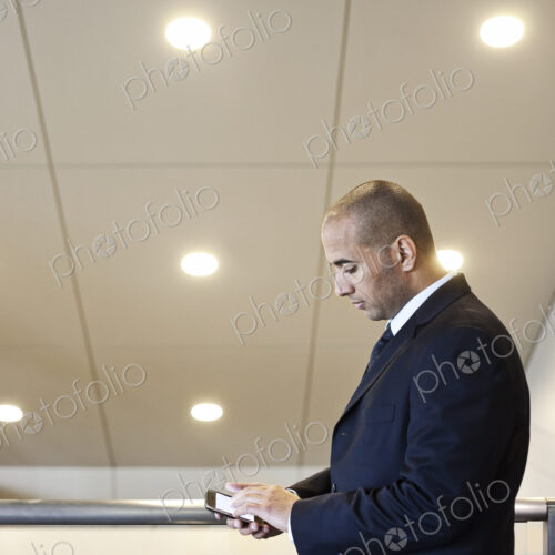 A middle eastern businessman working on a notebook computer standing in an office lobby. A middle eastern businessman working on a notebook computer standing in an office lobby.
