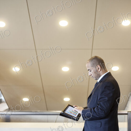 A middle eastern businessman working on a notebook computer standing in an office lobby. A middle eastern businessman working on a notebook computer standing in an office lobby.