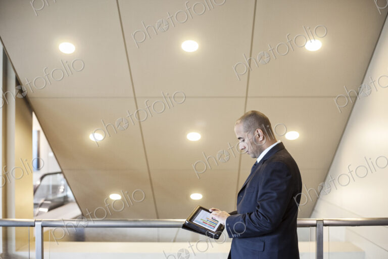 A middle eastern businessman working on a notebook computer standing in an office lobby.