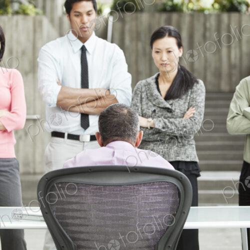 A mixed race group of business people standing in front of a person at a desk. A mixed race group of business people standing in front of a person at a desk.