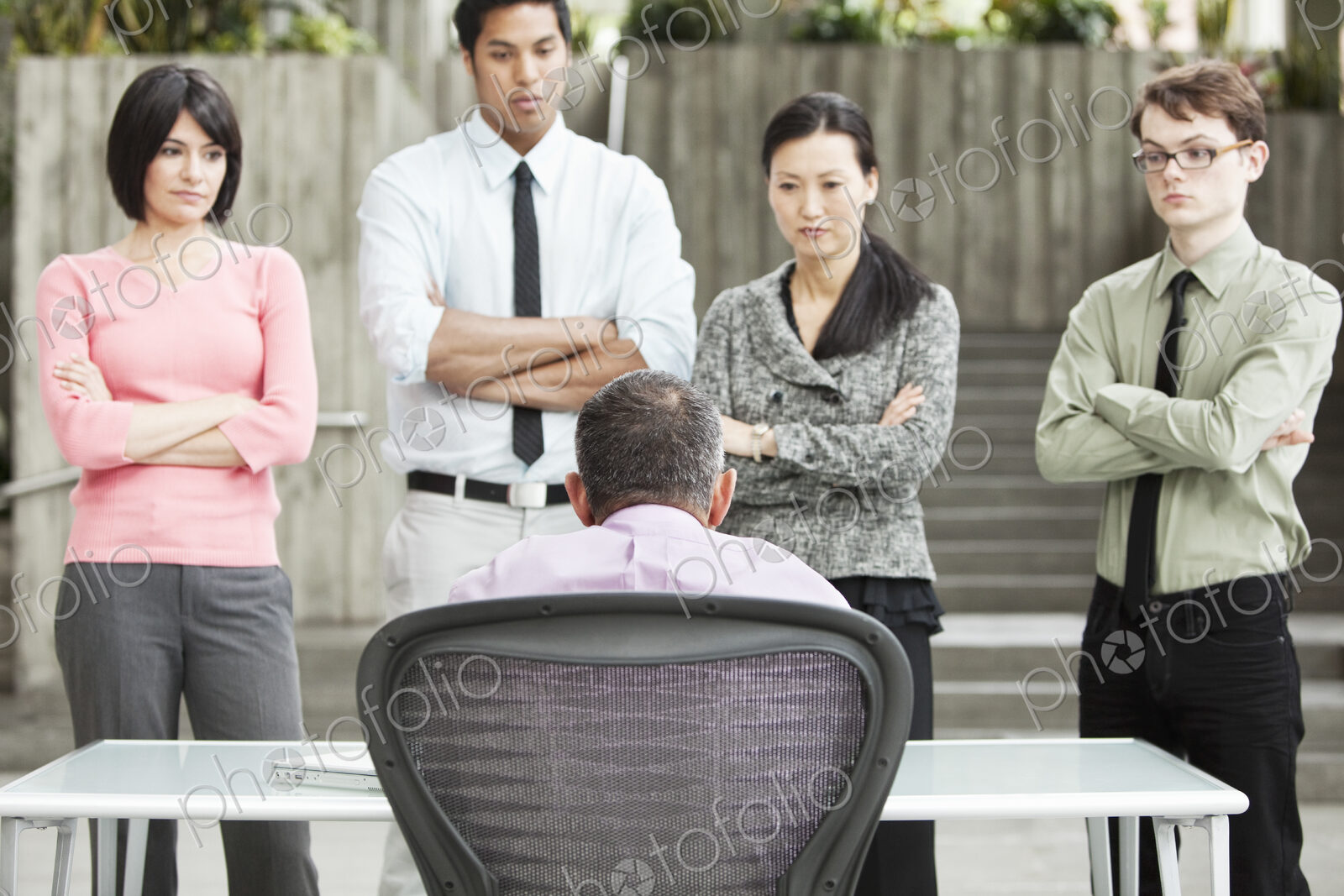 A mixed race group of business people standing in front of a person at a desk.