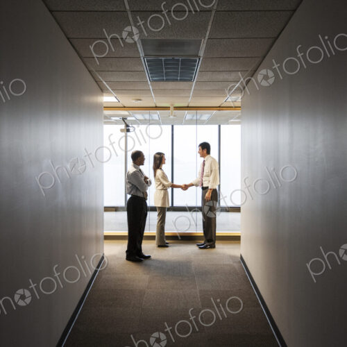 A mixed race group of business people talking and shaking hands in front of a window… A mixed race group of business people talking and shaking hands in front of a window…