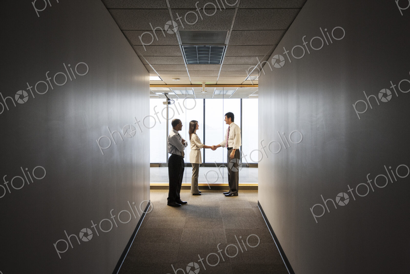 A mixed race group of business people talking and shaking hands in front of a window…