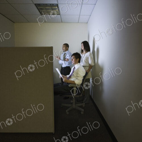 A mixed race group of three business people lit up by a desktop computer screen in a… A mixed race group of three business people lit up by a desktop computer screen in a…