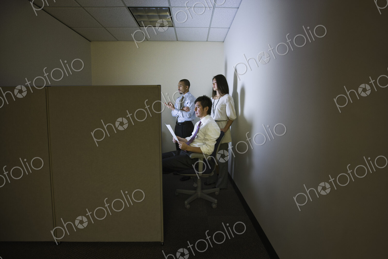 A mixed race group of three business people lit up by a desktop computer screen in a…