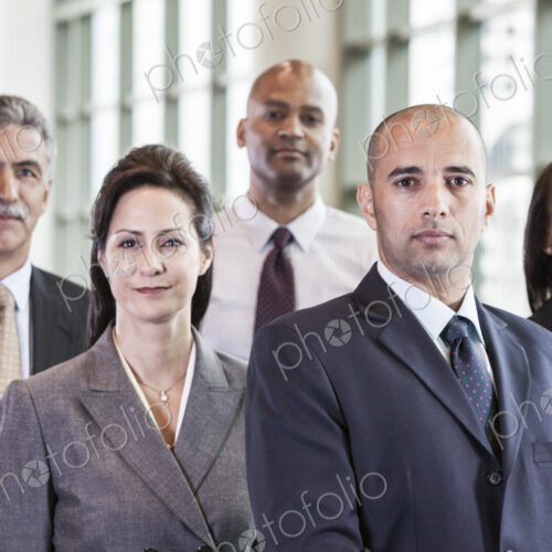 A mixed race group portrait of business people standing in a convention center lobby. A mixed race group portrait of business people standing in a convention center lobby.