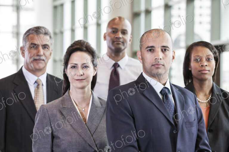 A mixed race group portrait of business people standing in a convention center lobby.