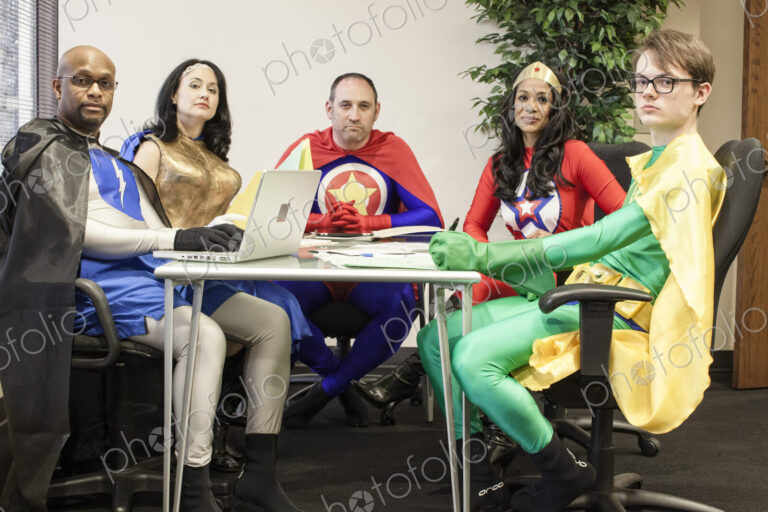 A mixed race team of office super heros sitting at a table in a planning meeting.