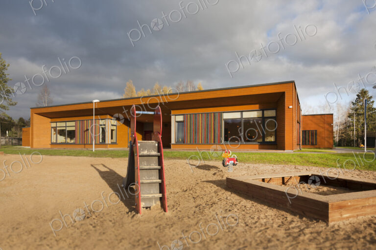 A modern building, nursery or pre-school, a large sand pit play area with a slide.