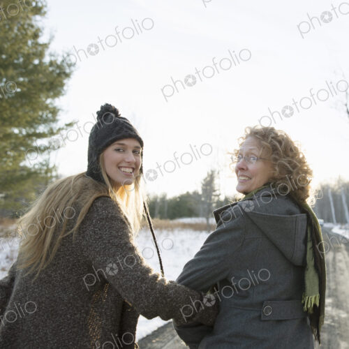 A mother and daughter arm in arm walking along a path and looking over their shoulders.