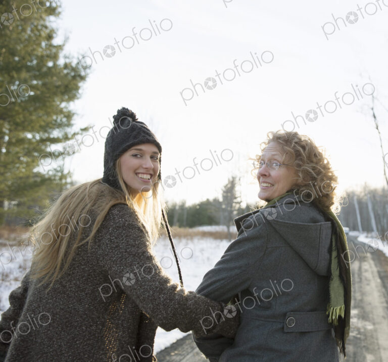 A mother and daughter arm in arm walking along a path and looking over their shoulders.
