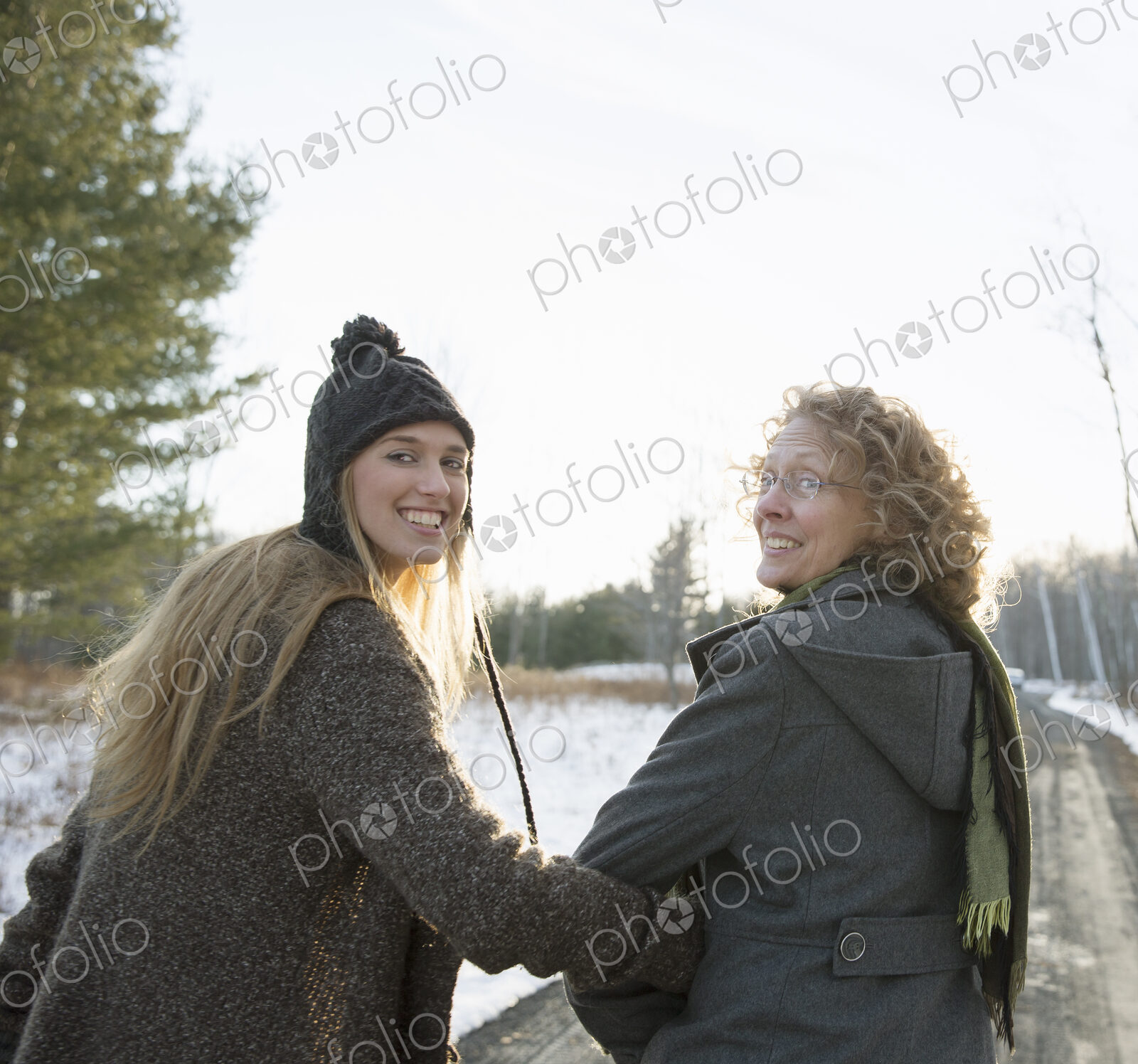 A mother and daughter arm in arm walking along a path and looking over their shoulders.