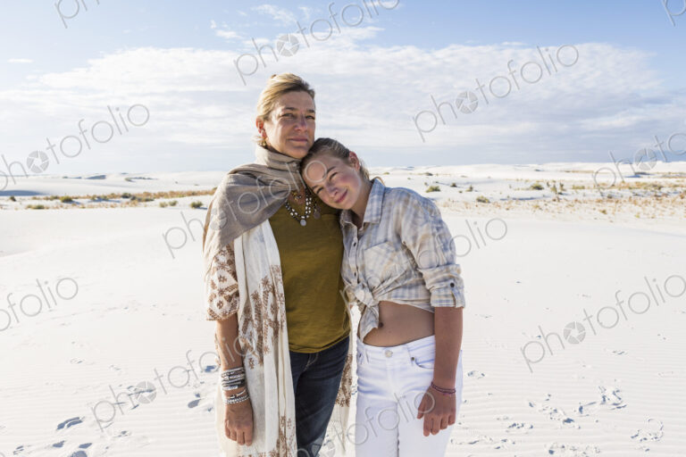 A mother and her teenage daughter side by side, arms around waists, in an open space