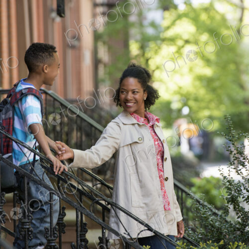 A mother and son, a woman and a boy on a flight of steps outside a brownstone building.