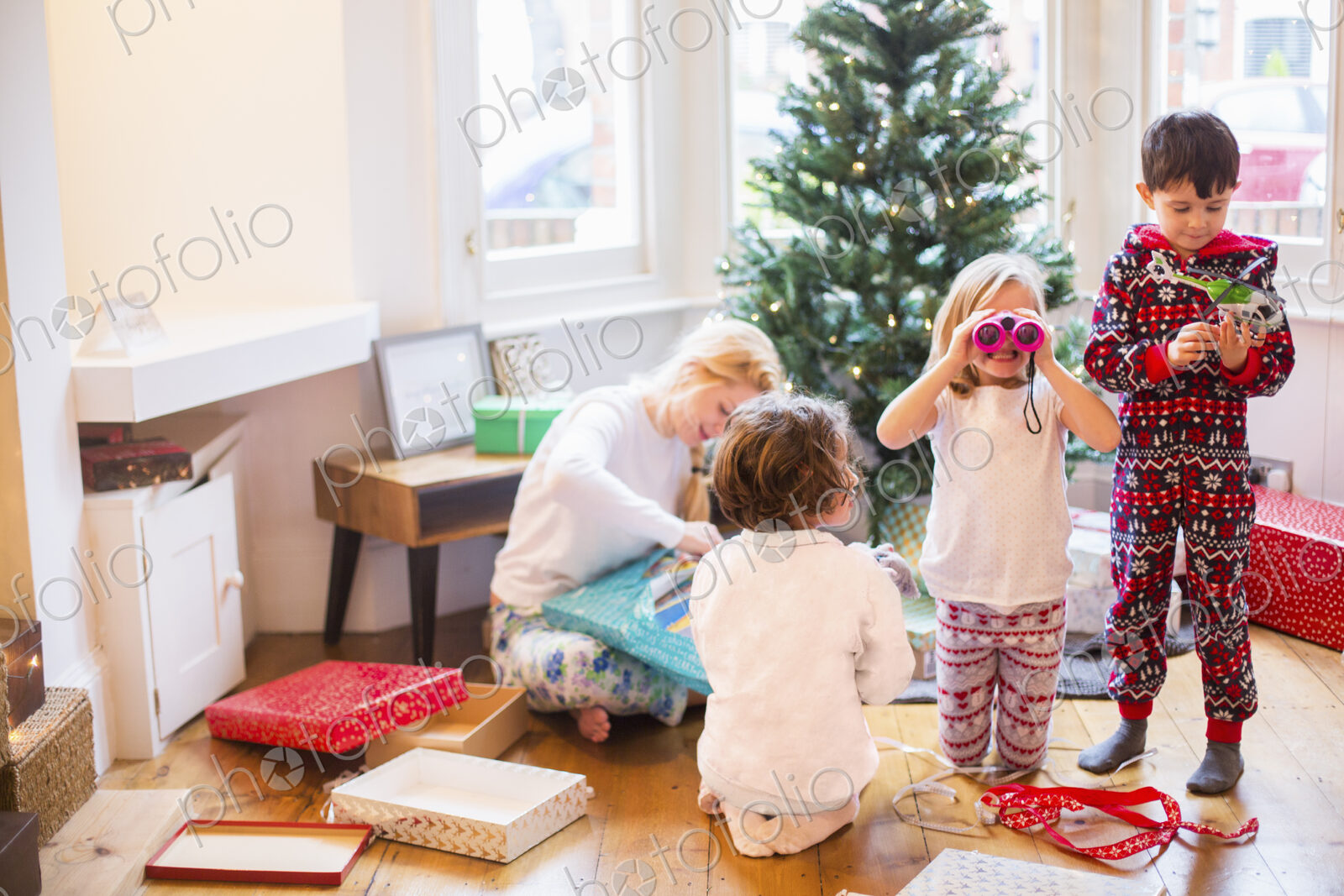 A mother and three children on Christmas morning opening presents.