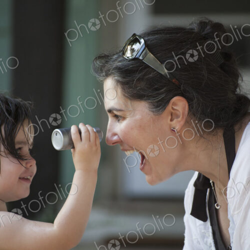 A mother and young daughter face to face, playing and laughing.