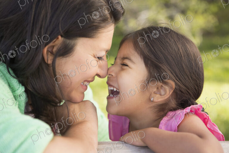 A mother in the park with her daughter, laughing and kissing each other.