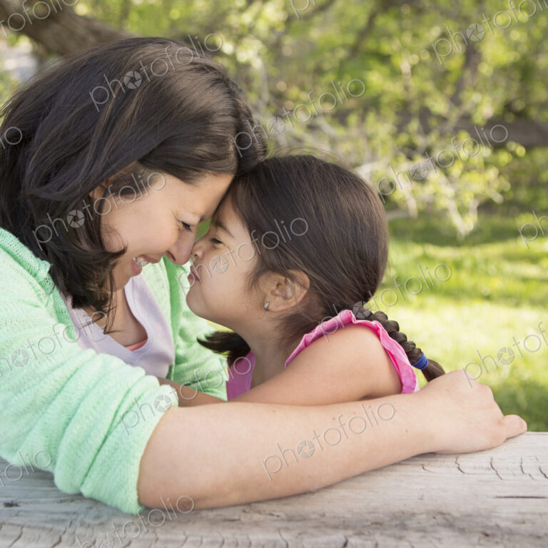 A mother in the park with her daughter, laughing and kissing each other.