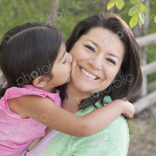 A mother in the park with her daughter, laughing and kissing each other.