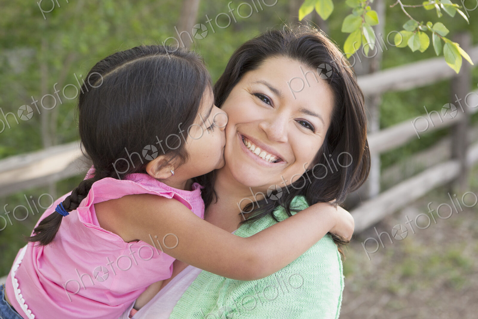 A mother in the park with her daughter, laughing and kissing each other.