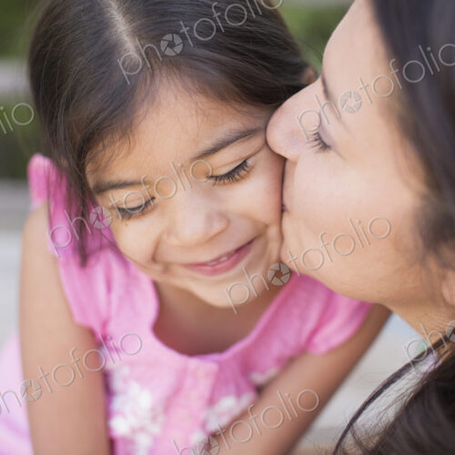 A mother in the park with her daughter, laughing and kissing each other.