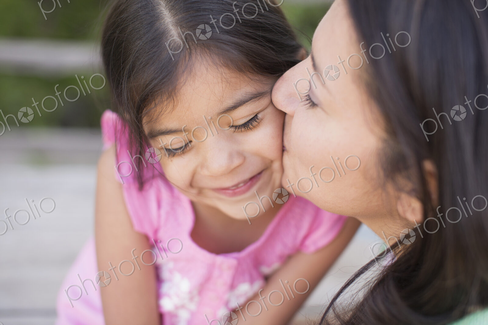 A mother in the park with her daughter, laughing and kissing each other.