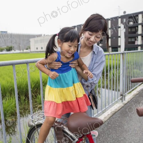 A mother lifting her daughter onto a bicycle.