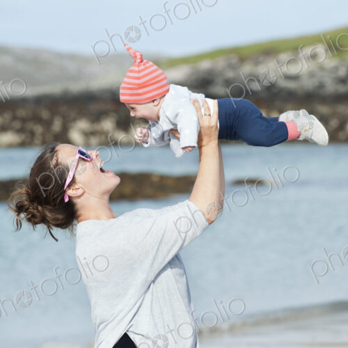 A mother raising her baby in the air. At the seaside. A mother raising her baby in the air. At the seaside.